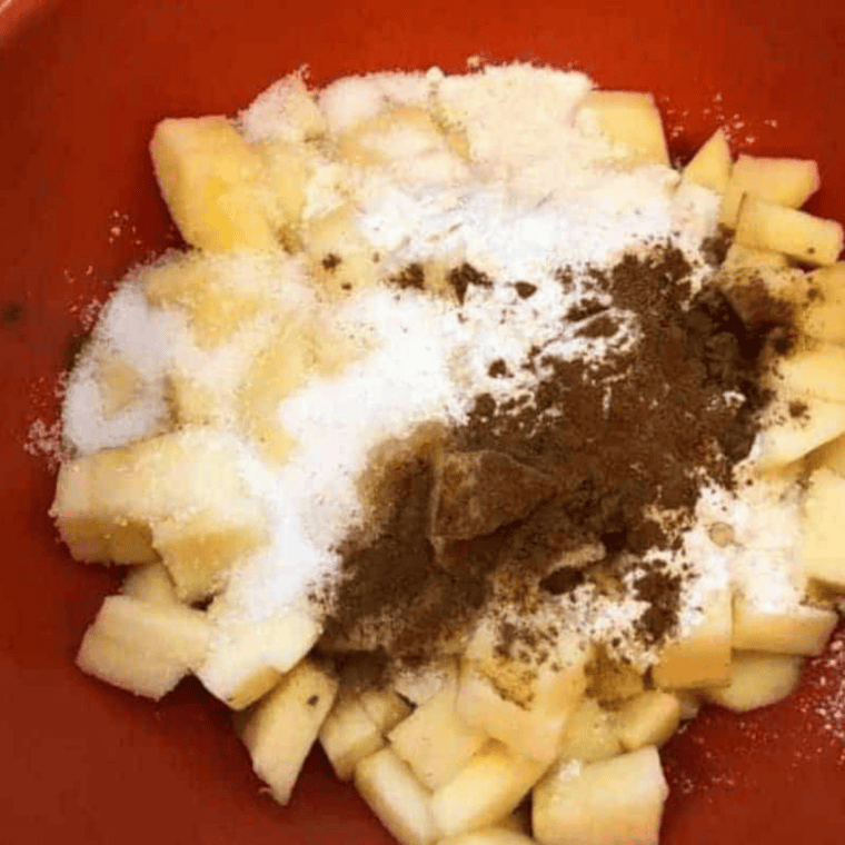 Diced apples tossed with sugar, flour, cinnamon, and vanilla in a glass mixing bowl
