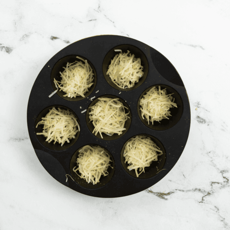 Spray muffin tin with olive oil and add shredded Parmesan cheese.