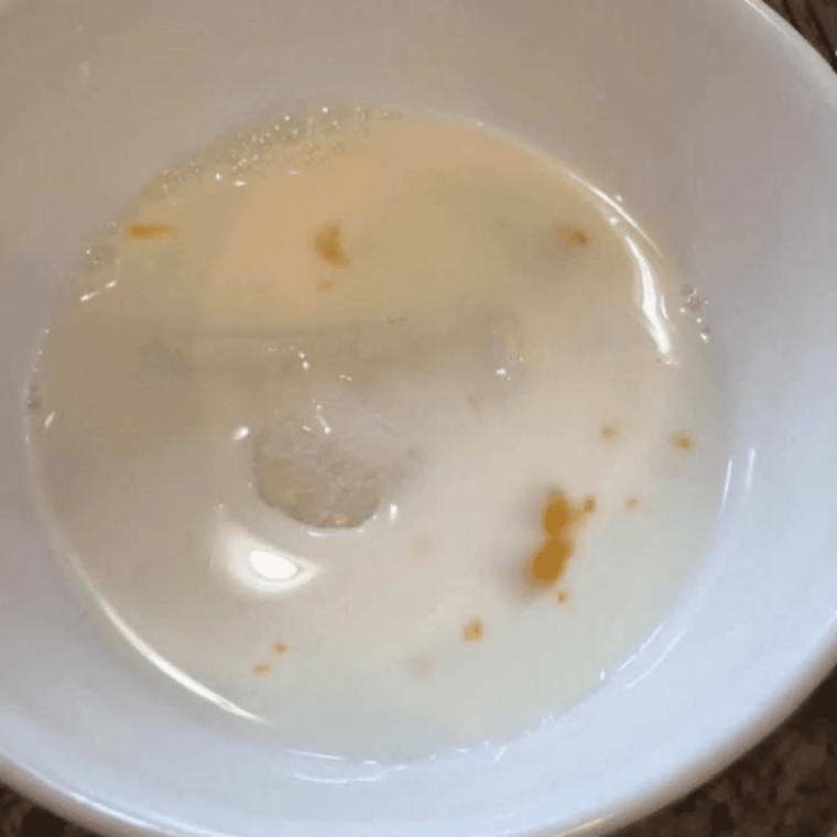 Egg and milk mixture in a bowl with pierogies soaking before breading.