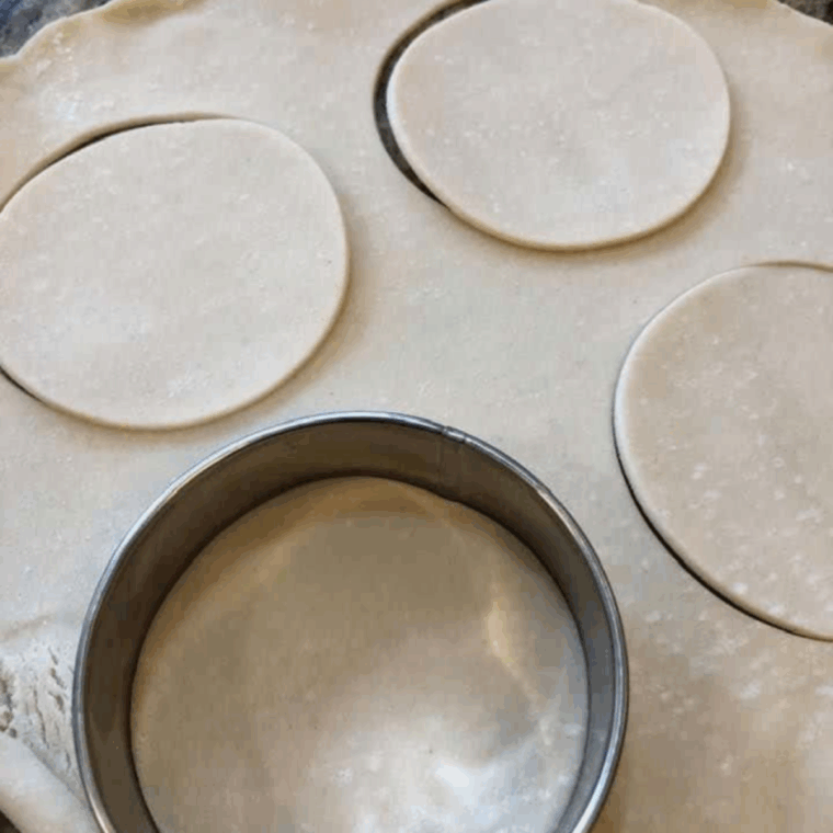 Rolling out dough on a floured surface and cutting circles with biscuit cutters larger than muffin tin holes.