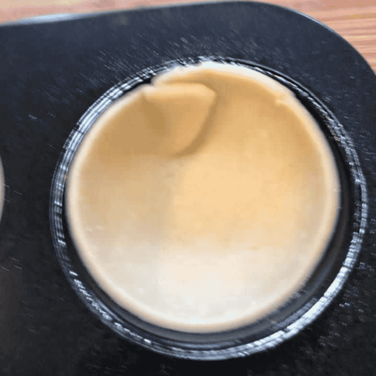 Pressing dough into a muffin tin and filling each cup with peach pie filling.