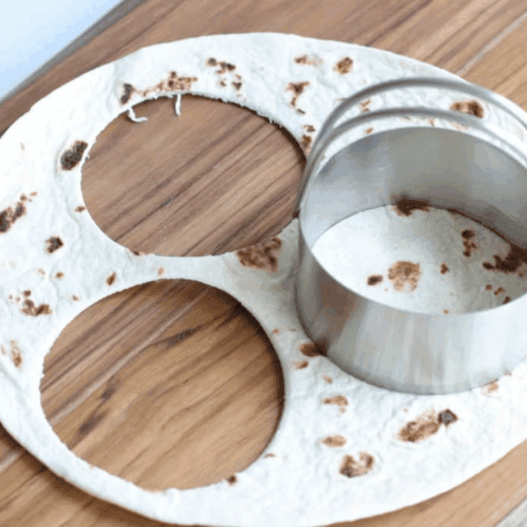 Flour tortilla being cut into small circles with a biscuit cutter, ready for air frying.