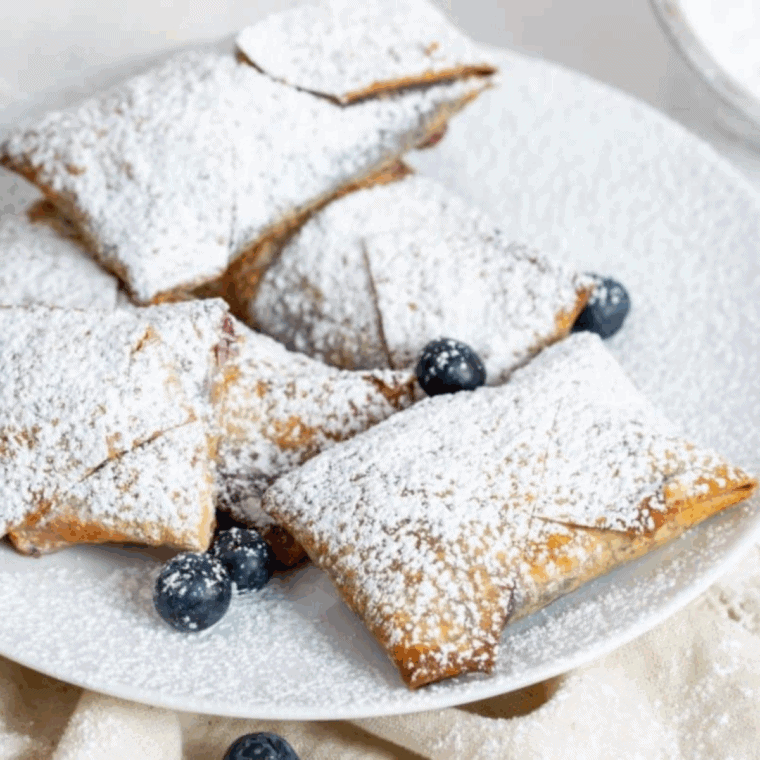 Golden air fryer blueberry cheesecake egg rolls with crispy wrappers and creamy blueberry filling, dusted with powdered sugar.