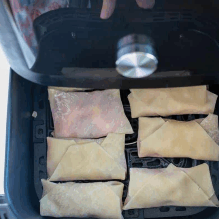 Sealed egg rolls brushed with water, sprayed with olive oil, placed in air fryer, cooked until golden, and dusted with powdered sugar.