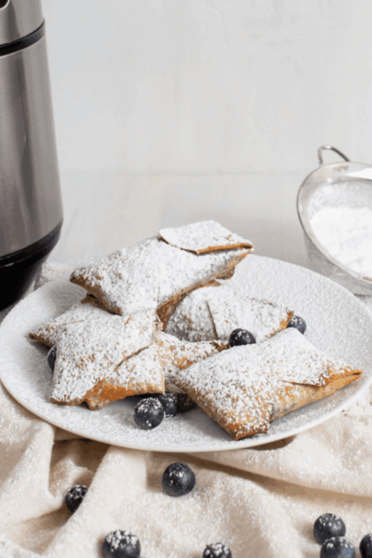Golden air fryer blueberry cheesecake egg rolls with powdered sugar, crispy and creamy dessert ready to serve.
