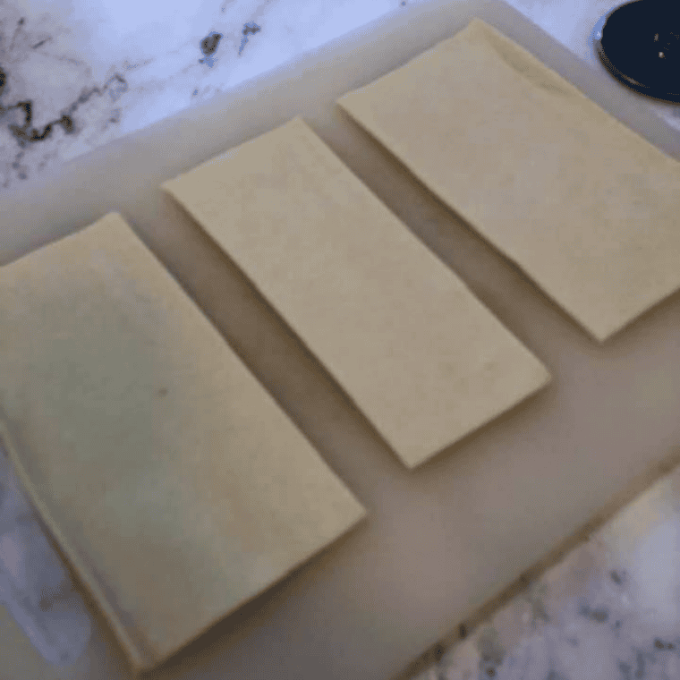 Puff pastry sheet cut into six equal squares on a cutting board
