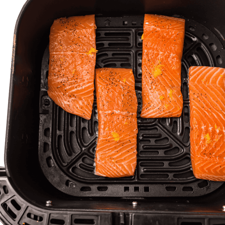 Raw salmon fillets placed skin-side down in an air fryer basket to cook at 400°F