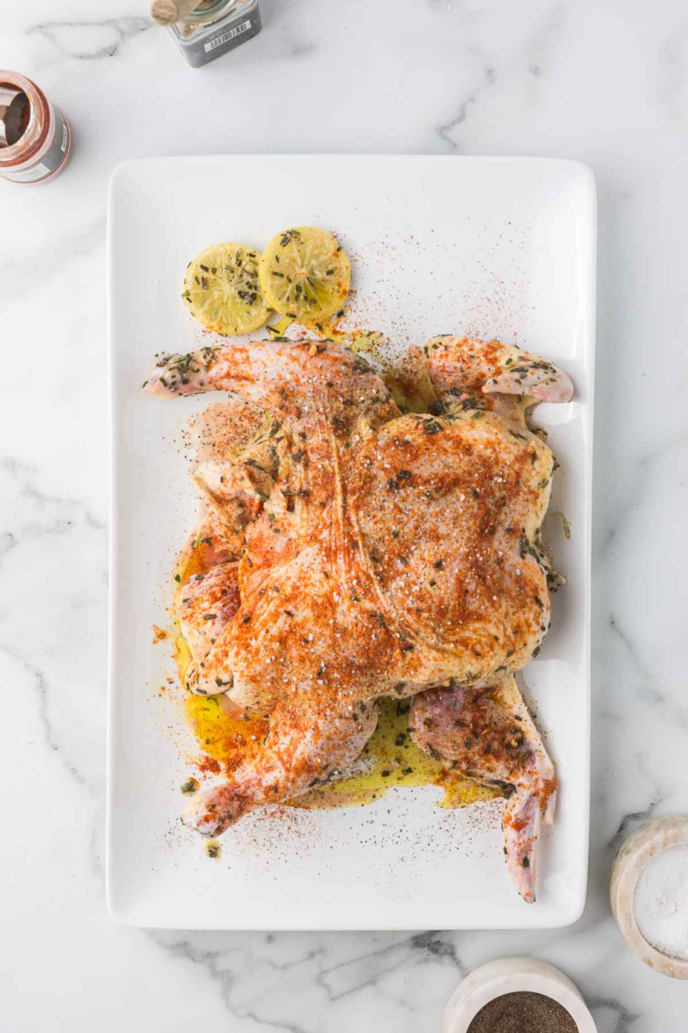 Seasoned spatchcock chicken on a white plate.