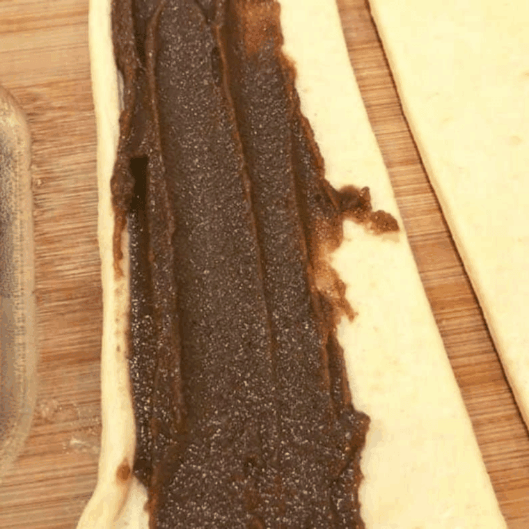 small bowl of apple butter, brown sugar, and flour mixture being spread onto crescent dough rectangles
