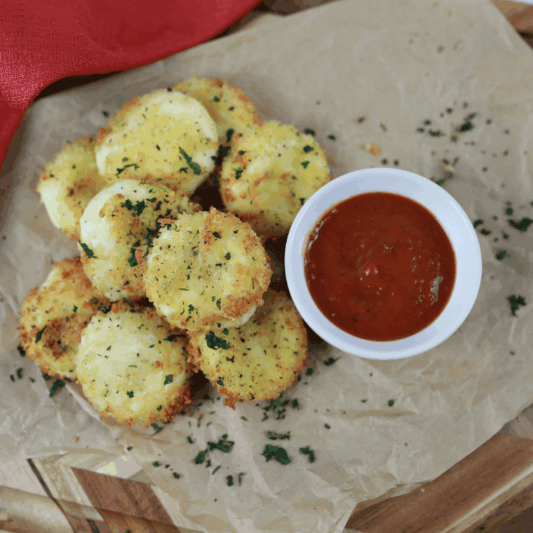 Crispy golden Air Fryer Babybel cheese being pulled apart to show the melted, gooey interior, next to a bowl of marinara sauce.