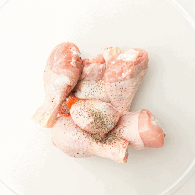 Raw chicken drumsticks being tossed with Cajun marinade ingredients in a large mixing bowl.