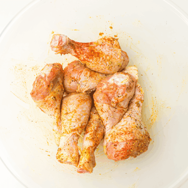 Closeup of chicken legs evenly coated in vibrant Cajun seasoning, olive oil, and lemon juice.