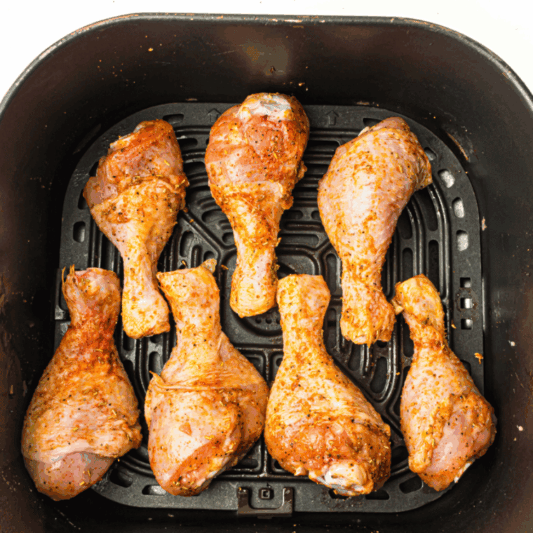 Marinated Cajun chicken drumsticks arranged neatly in a single layer in the air fryer basket.