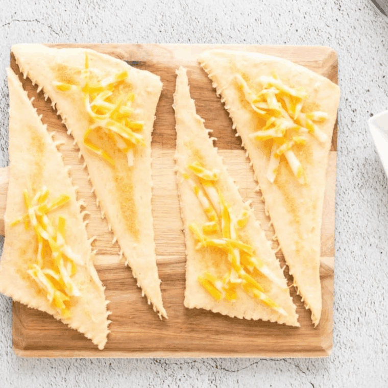 Laying out crescent dough and brushing it with a melted butter, garlic powder, and Italian seasoning mixture before filling.