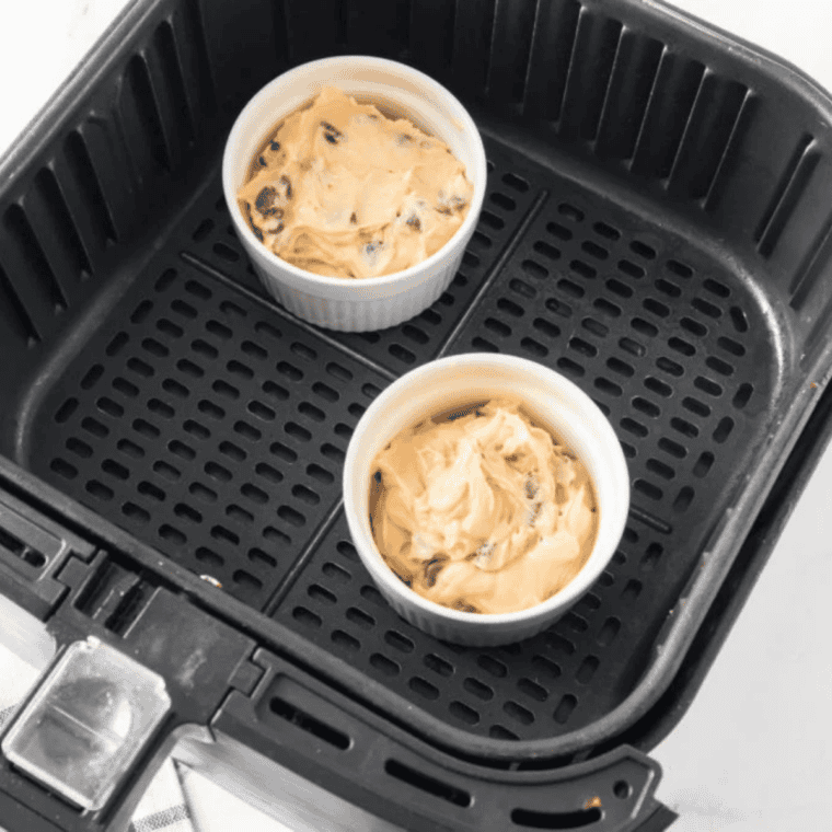 Two ramekins of chocolate chip cookie dough baking in an air fryer basket.