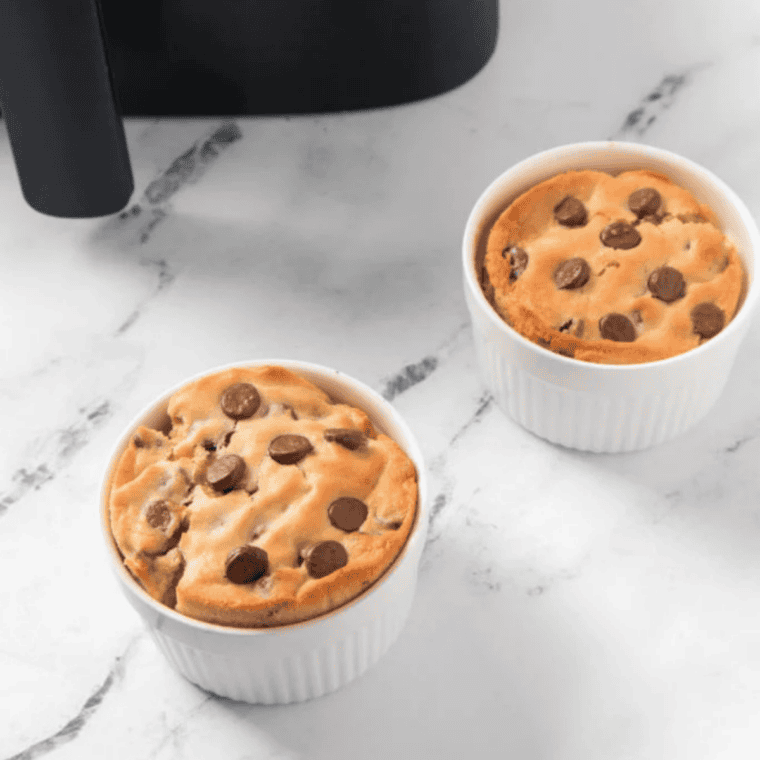 Gooey chocolate chip cookie baked in a mug using an air fryer, topped with melted chocolate chips.
