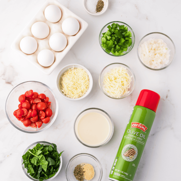 Ingredients for air fryer frittata: eggs, milk, diced bell peppers, onion, shredded cheddar, Italian seasoning, salt, and pepper in small bowls