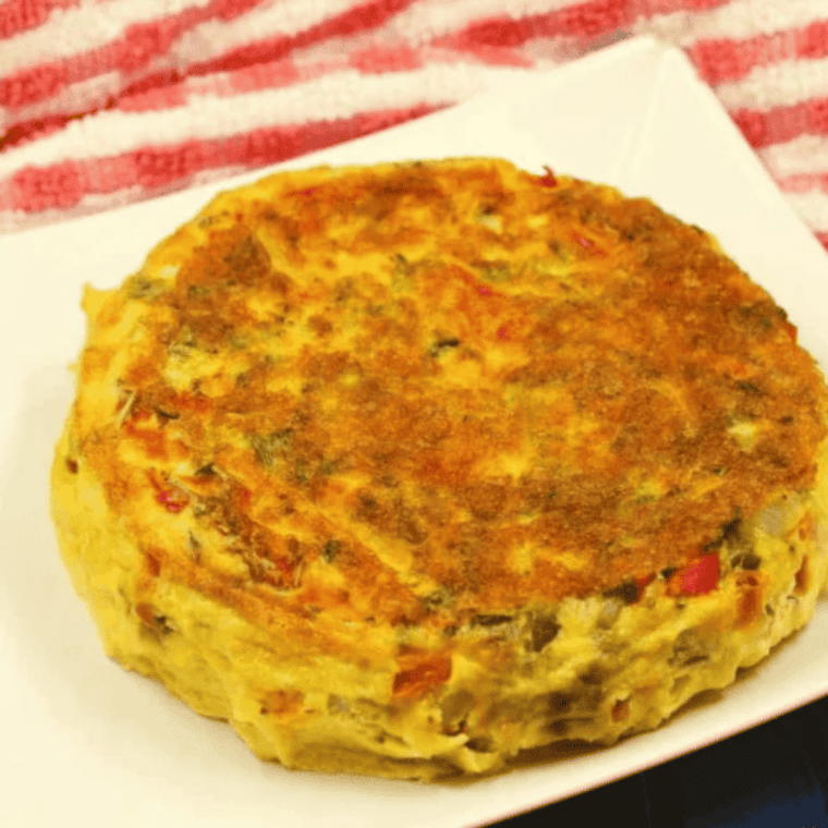 Cooked air fryer frittata resting in the pan, pulled away from the edges and sliced into wedges