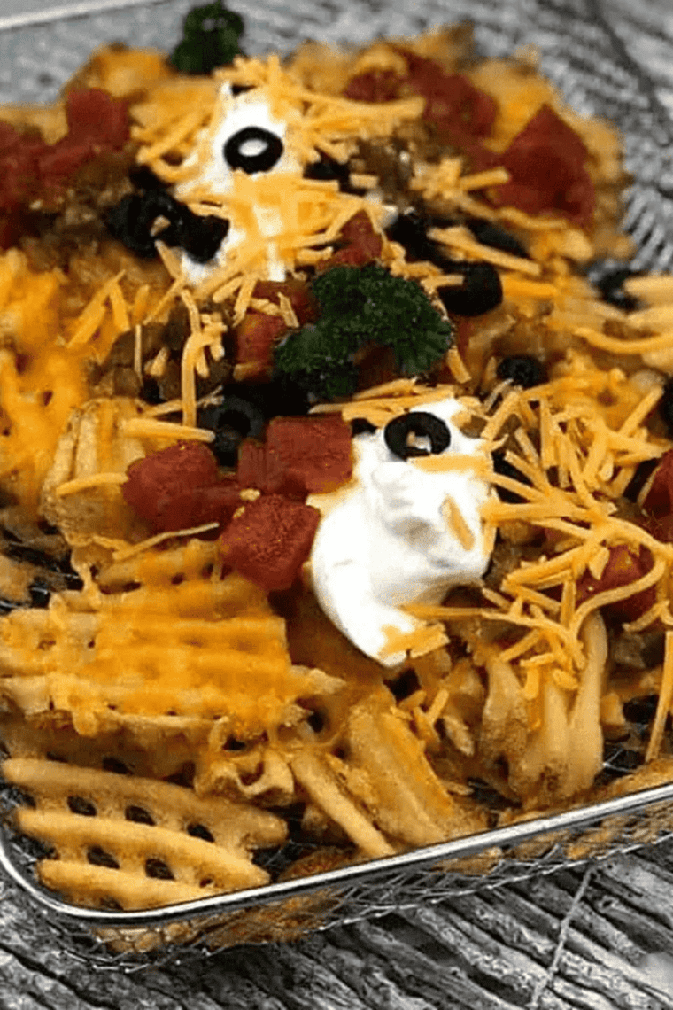 Sheet pan of loaded waffle fries with melted cheese, bacon, sour cream, guacamole, and diced tomatoes