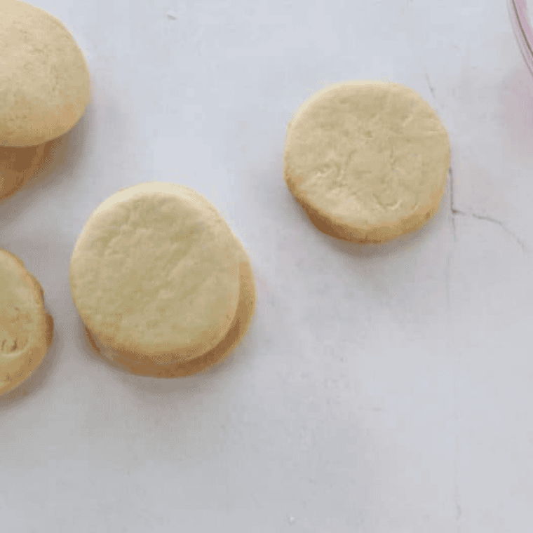 White frosting being spooned around the base of a marshmallow on a cookie to create a realistic "melted snow" puddle.