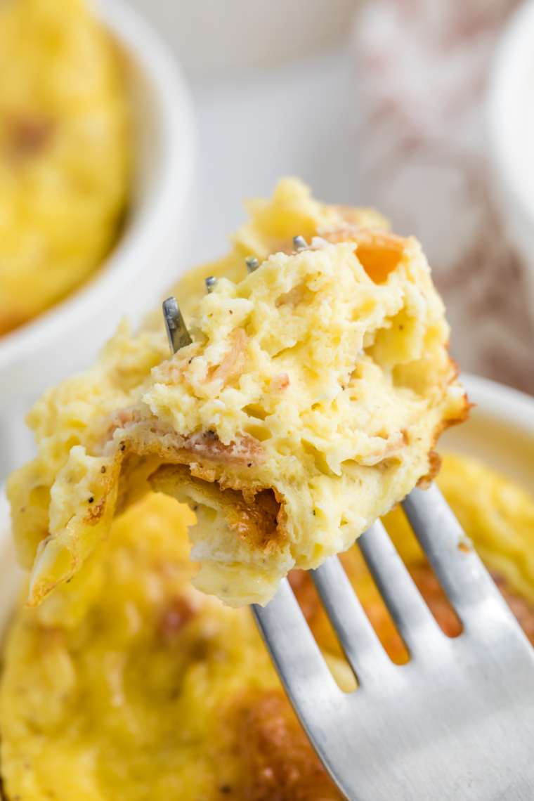 Golden cheesy egg mug omelet puffed up in a white ceramic ramekin, topped with melted cheddar and fresh green onions