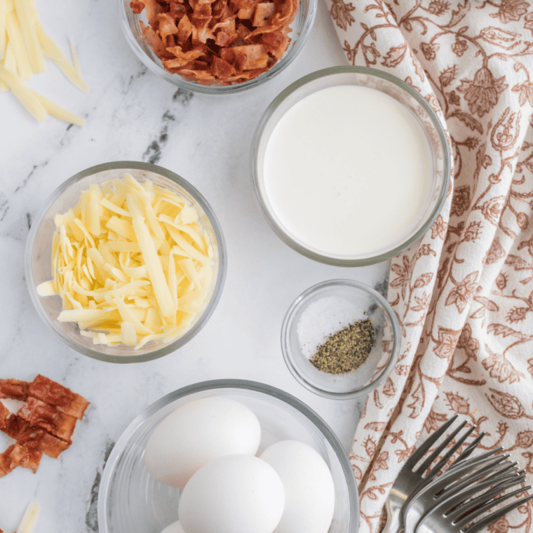 Ingredients for air fryer mug omelet: eggs, shredded cheddar cheese, scallions, milk, butter, dried thyme, salt, and pepper