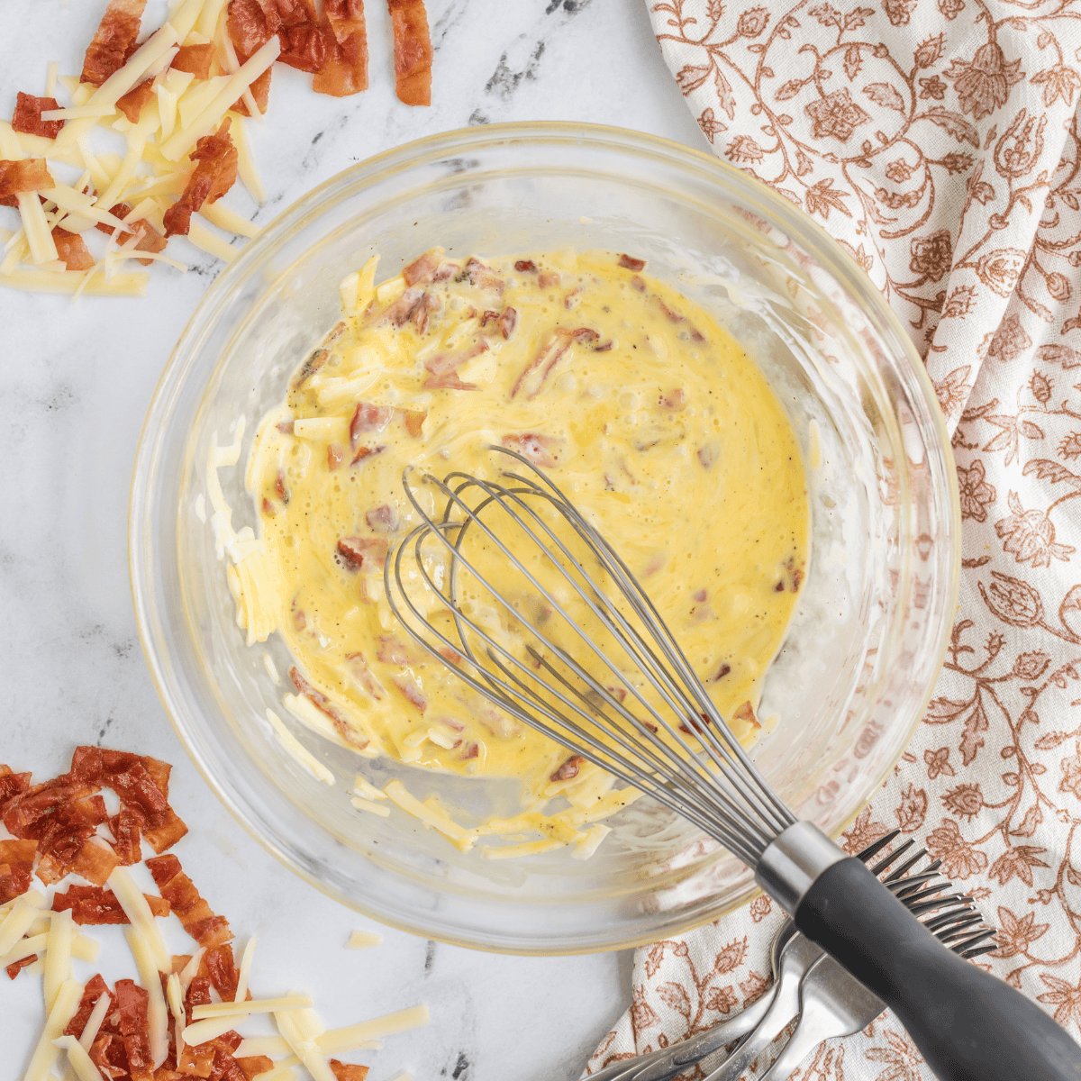Whisking eggs, milk, butter, and seasonings together in a glass bowl for an air fryer mug omelet