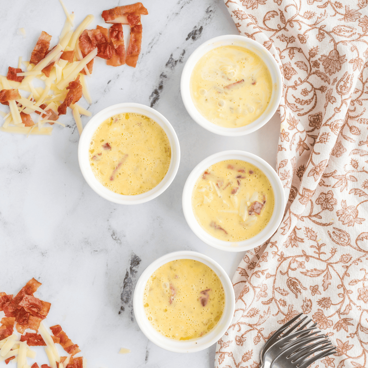 Pouring whisked egg mixture into a greased white ramekin and topping with shredded cheddar cheese for an air fryer mug omelet
