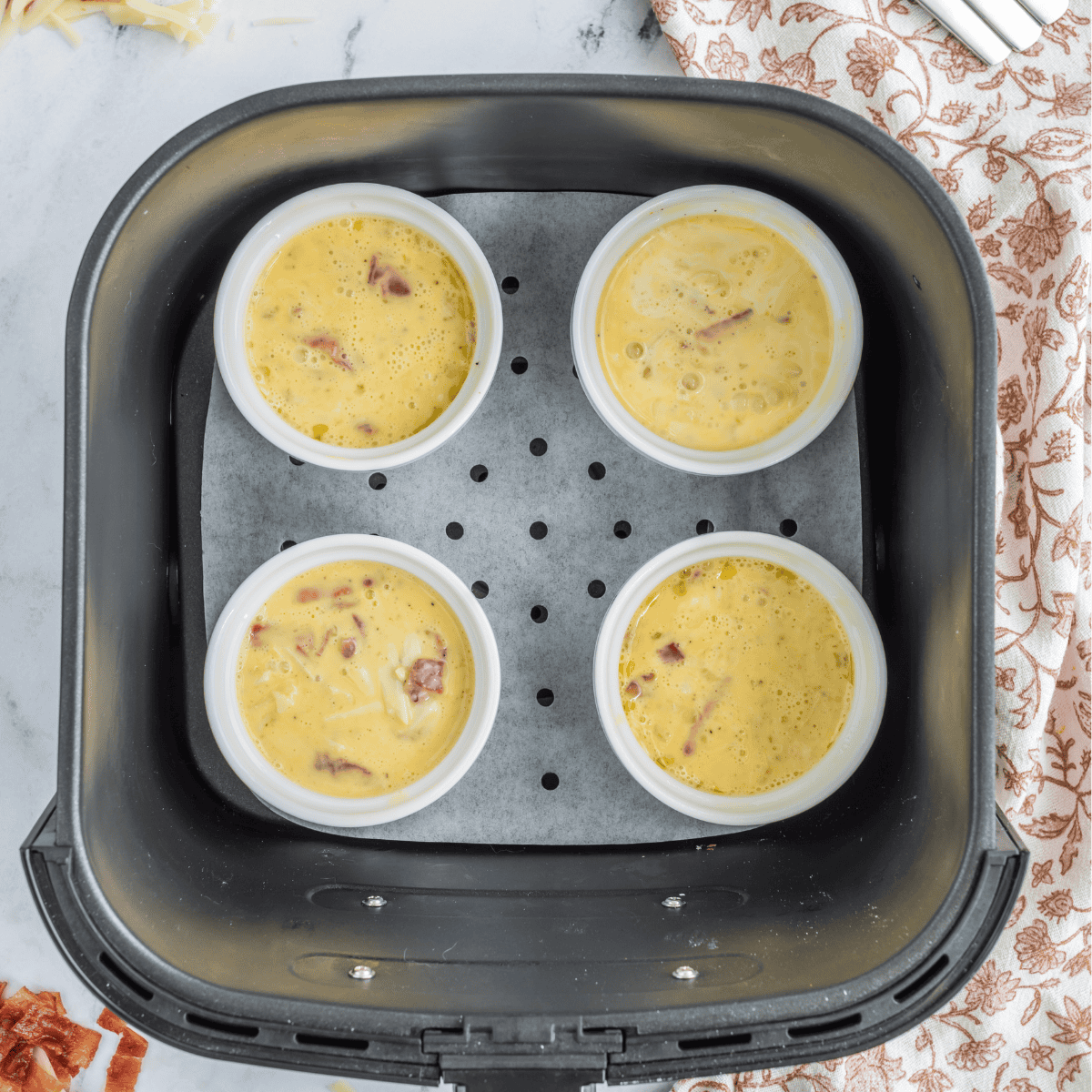 Ramekin filled with egg mixture placed inside an air fryer basket to cook at 330°F for 5 minutes