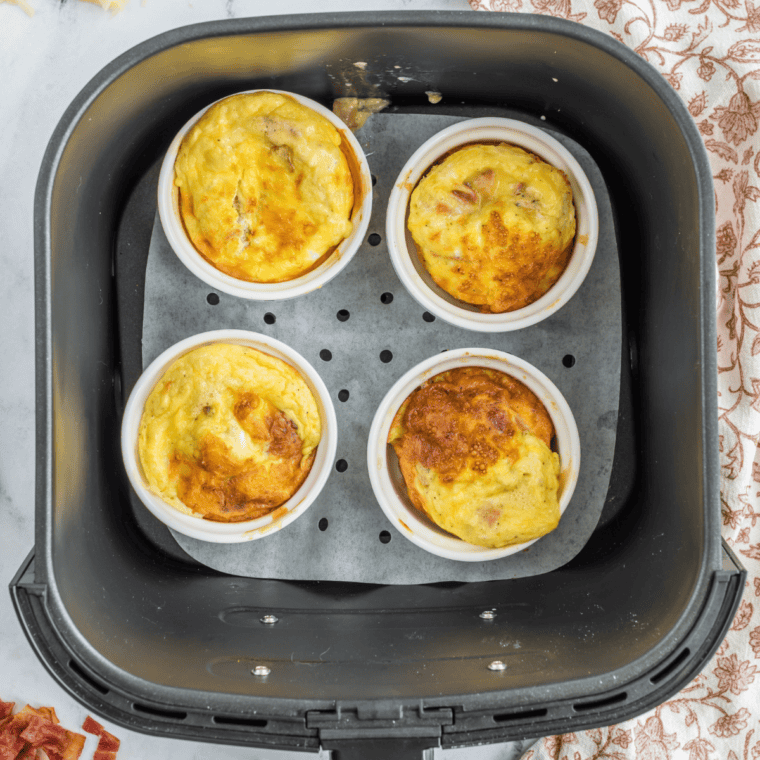 Finished air fryer mug omelet puffed and golden with melted cheddar cheese on top in a white ramekin