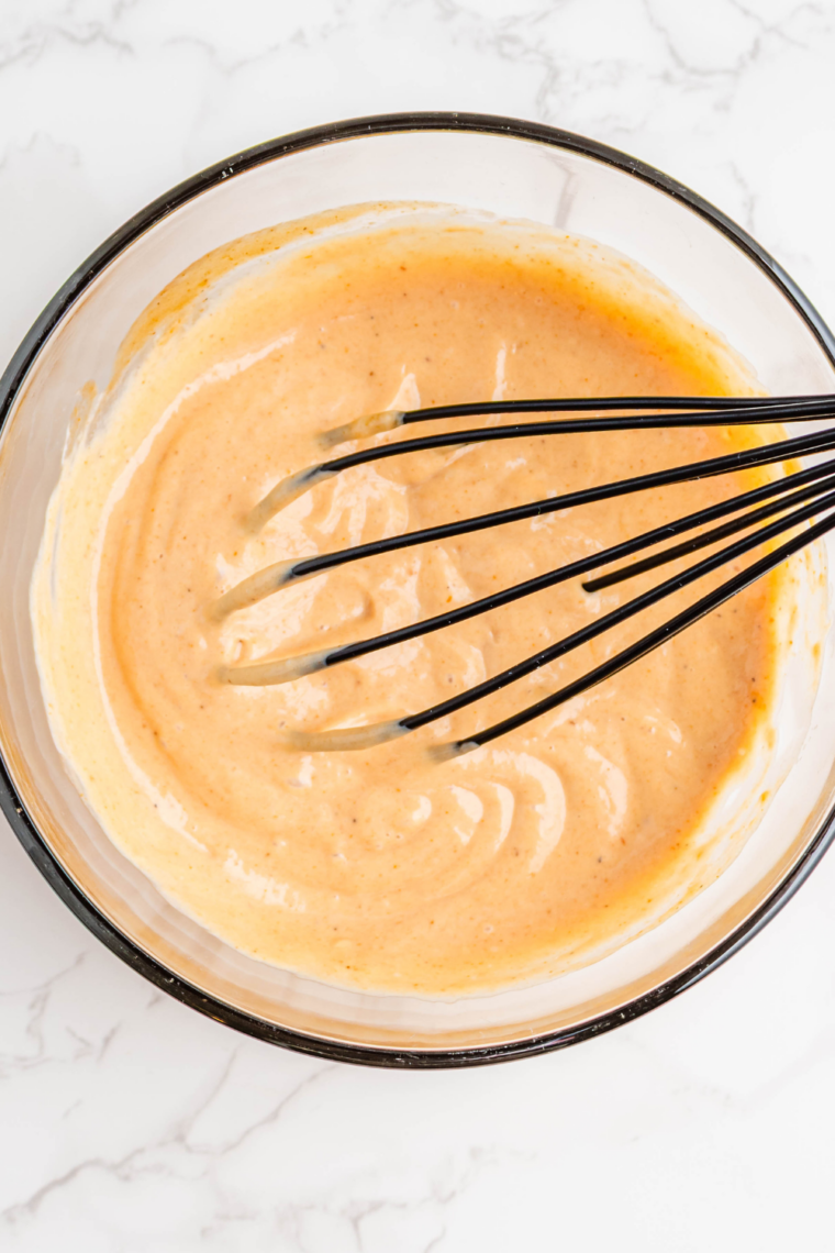 Whisked Cane’s sauce, smooth and pale orange with black pepper flecks
