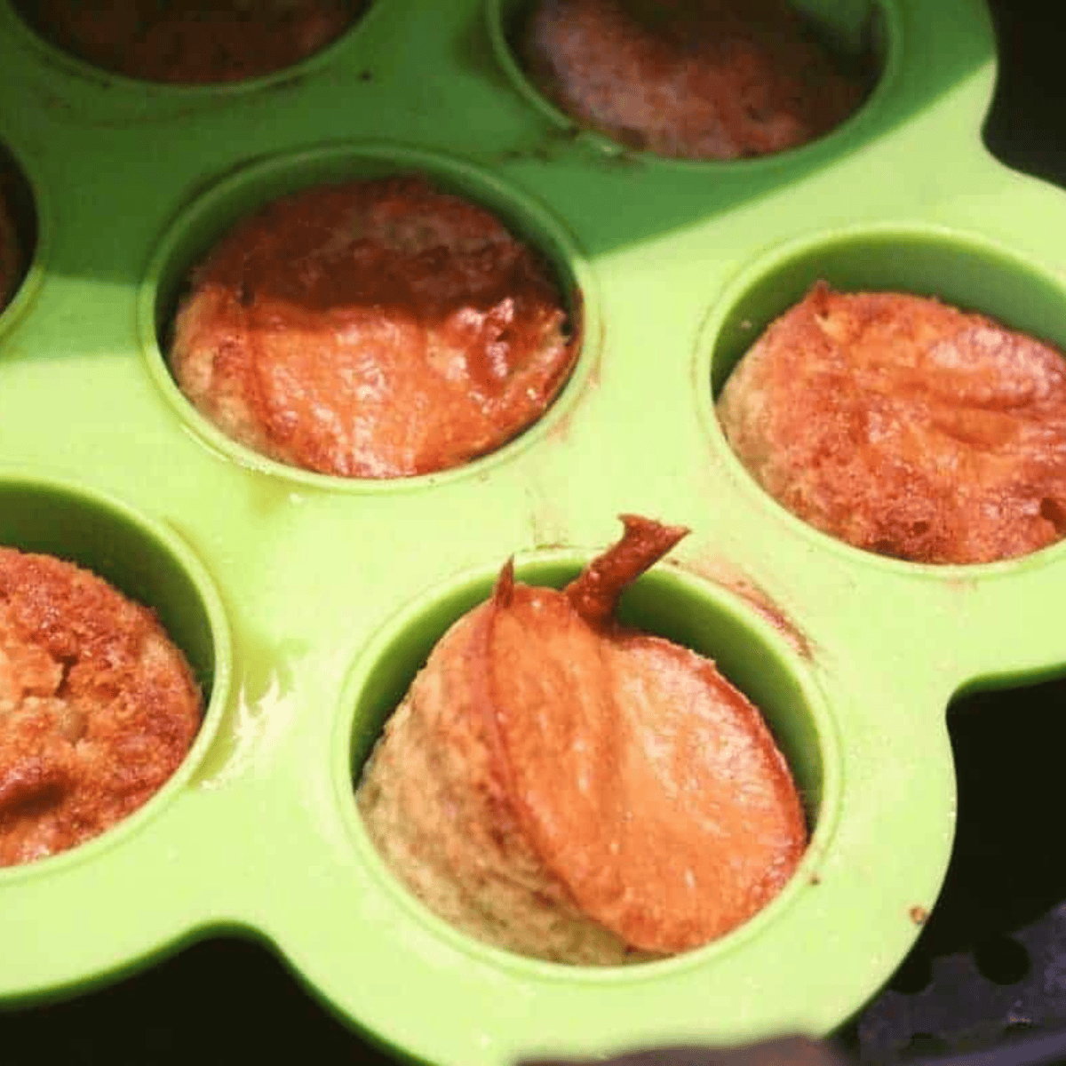 A rubber spatula folding flour into a dark molasses mixture before the mini-muffin tin is placed into a preheated oven.