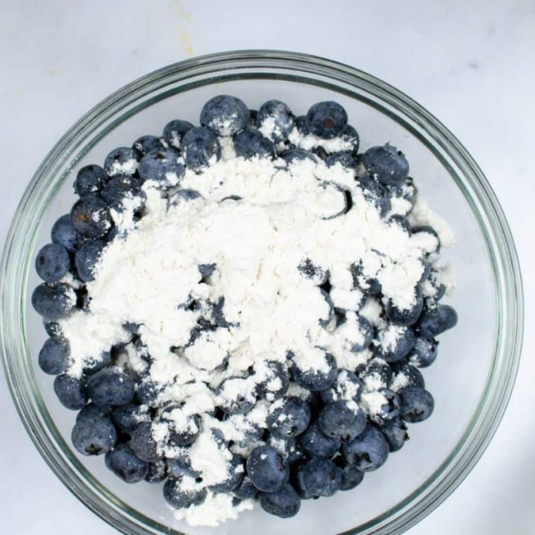 (Prep Your Blueberries): Blueberries tossed in flour inside a small bowl to prevent sinking in batter for even distribution in loaf.