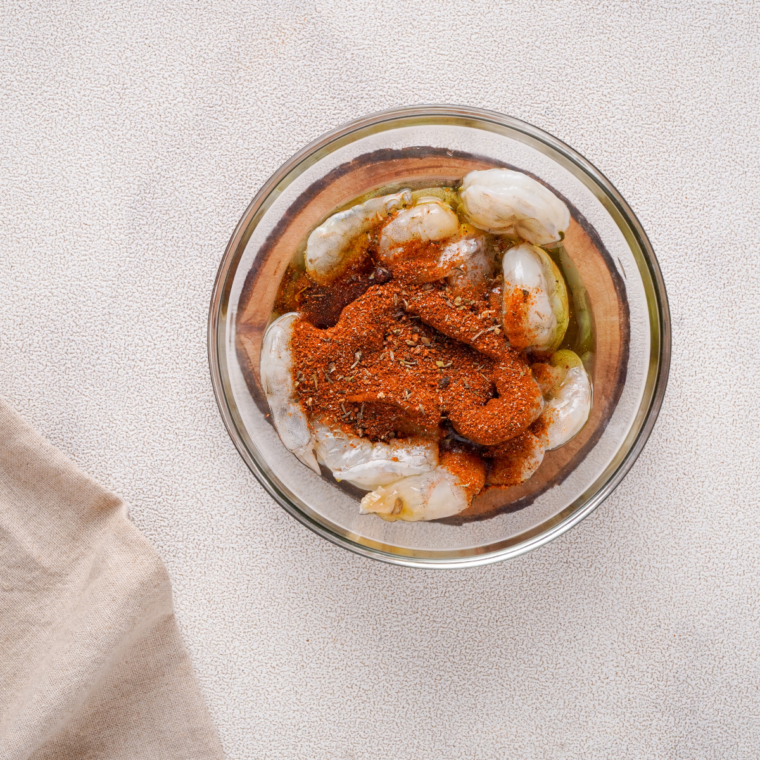 Raw shrimp tossed with oil and Cajun seasoning in a mixing bowl
