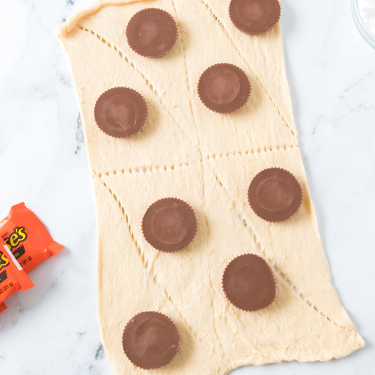 A frozen Reese&rsquo;s cup is placed on the dough and fully wrapped, then seams are tightly pinched shut to seal in the filling. The dough is shaped into a smooth ball to prevent any gaps where chocolate could escape.