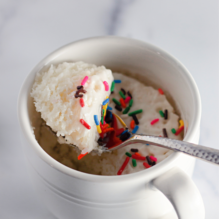 Air fryer vanilla mug cake with white icing and sprinkles in a white ceramic mug