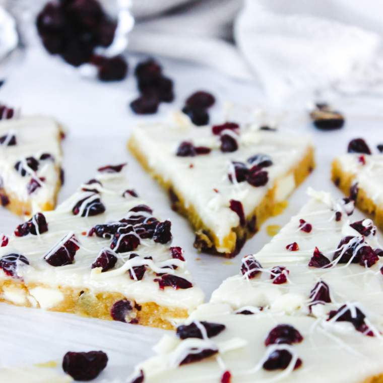 Air fryer cranberry bliss bars cut into triangles, topped with orange cream cheese frosting, dried cranberries, and white chocolate drizzle