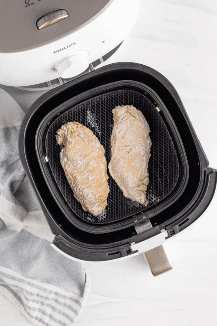 Breaded chicken breasts cooking in a preheated air fryer until golden brown and crispy, ready for a sandwich.