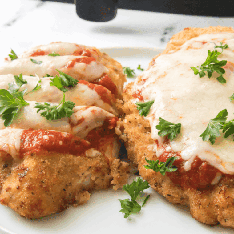 Crispy breaded chicken Parmesan topped with marinara sauce and melted mozzarella cheese on a white plate.