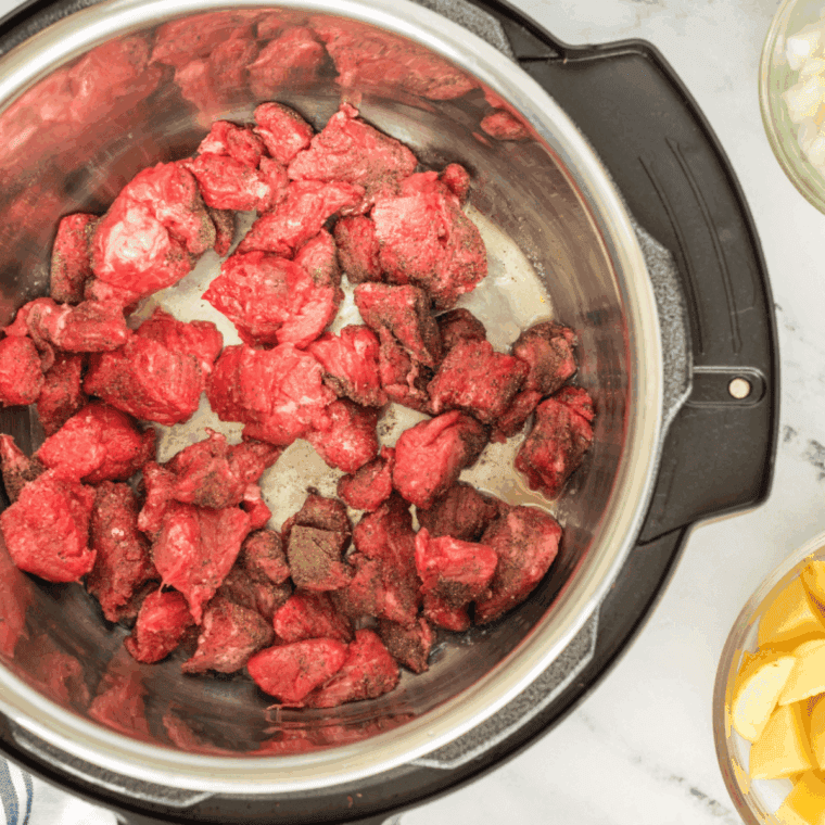Beef pieces coated with flour, salt, and pepper browning in butter in an Instant Pot using the sauté function.