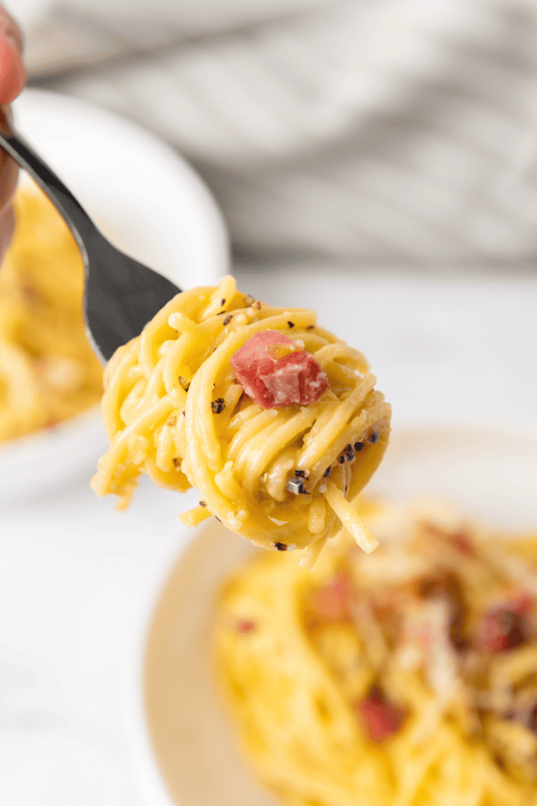 Fork twirling creamy carbonara pasta with bacon pieces and parmesan cheese.