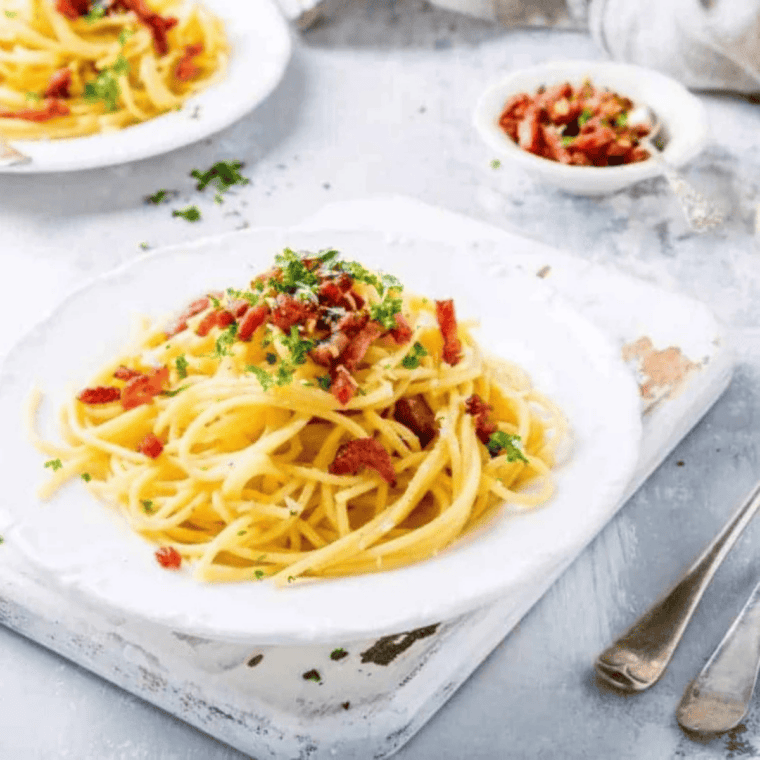 Finished Instant Pot pasta carbonara topped with crispy pancetta, black pepper, and fresh parsley