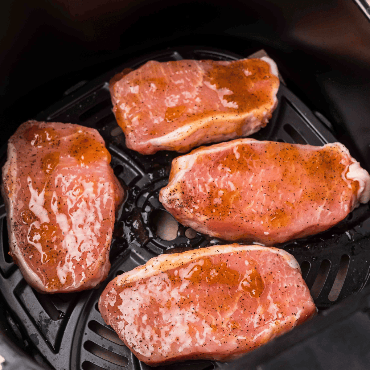 Frozen pork chops in a single layer in the air fryer basket before seasoning