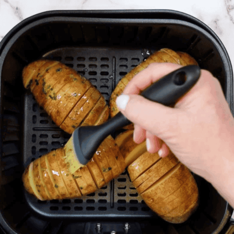 Brushing Hasselback potatoes with melted butter and seasoning garlic, salt, and black pepper between slices