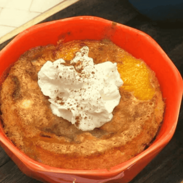 Air fryer peach cobbler served in a ramekin, topped with whipped cream and vanilla ice cream.
