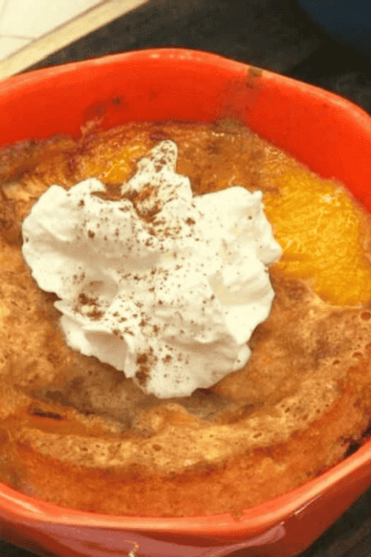 Individual ramekin of golden-brown peach cobbler cooked in an air fryer, topped with whipped cream or ice cream.
