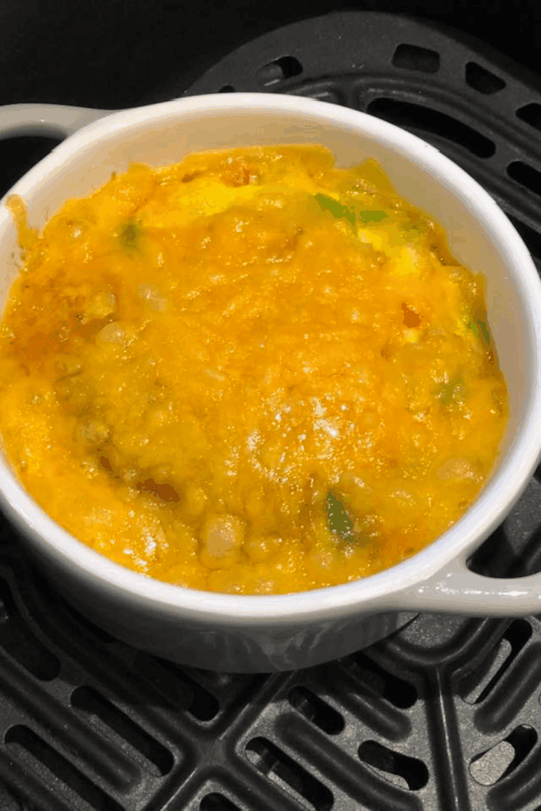 A fluffy air fryer vegetable omelet filled with bell peppers, onions, spinach, and melted cheese, served hot in a round air fryer pan on a white plate.