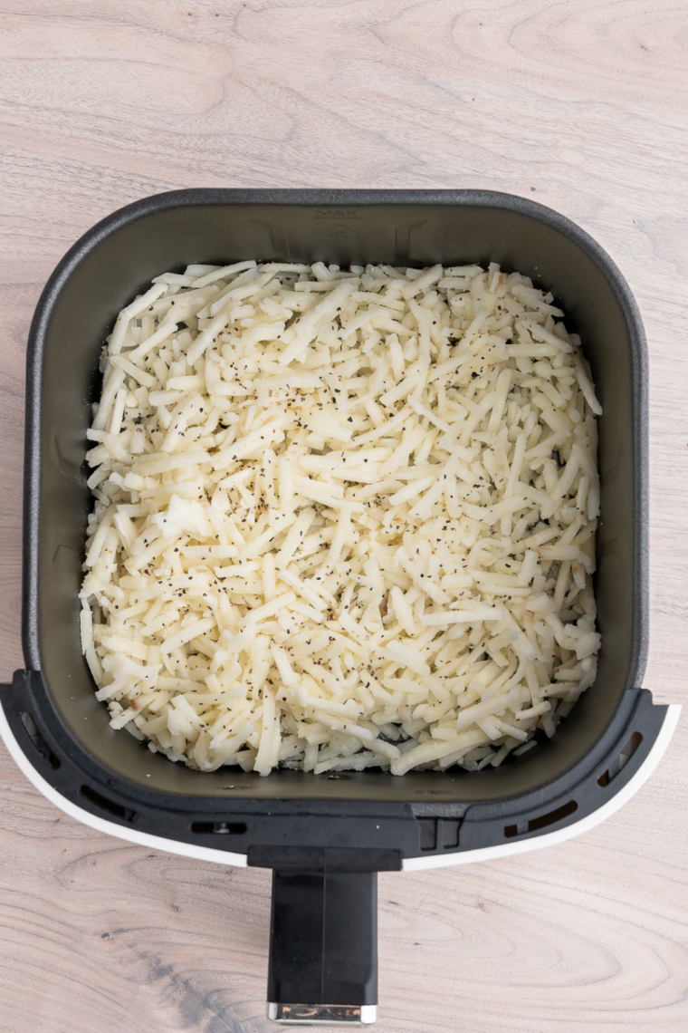 Frozen shredded hash browns being tossed in bowl with oil, garlic powder, salt, and pepper for even coating before air frying