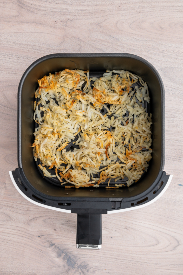 Shredded hash browns cooking in air fryer at 375&deg;F while being stirred halfway through for even crispiness and golden browning