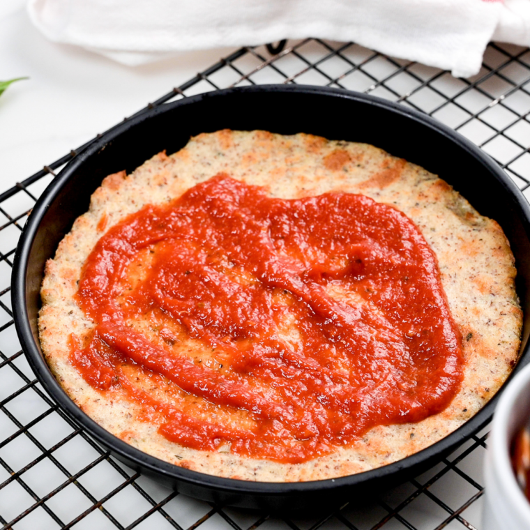 Air fryer pizza topped with a thin layer of sauce and shredded mozzarella